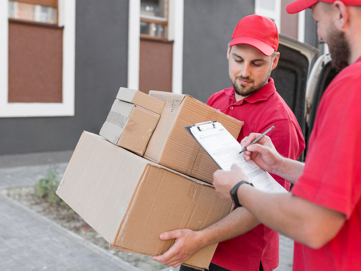 Two delivery men in red uniforms handling multiple packages and checking a delivery form, representing a parcel delivery service in Birmingham.