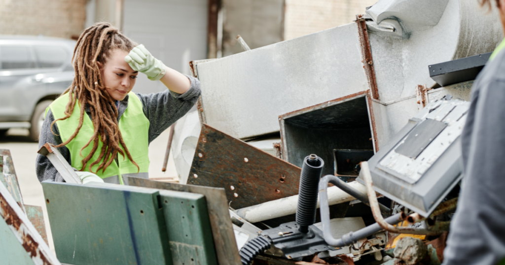 Person wearing a safety vest sorting through metal scrap for waste removal services.